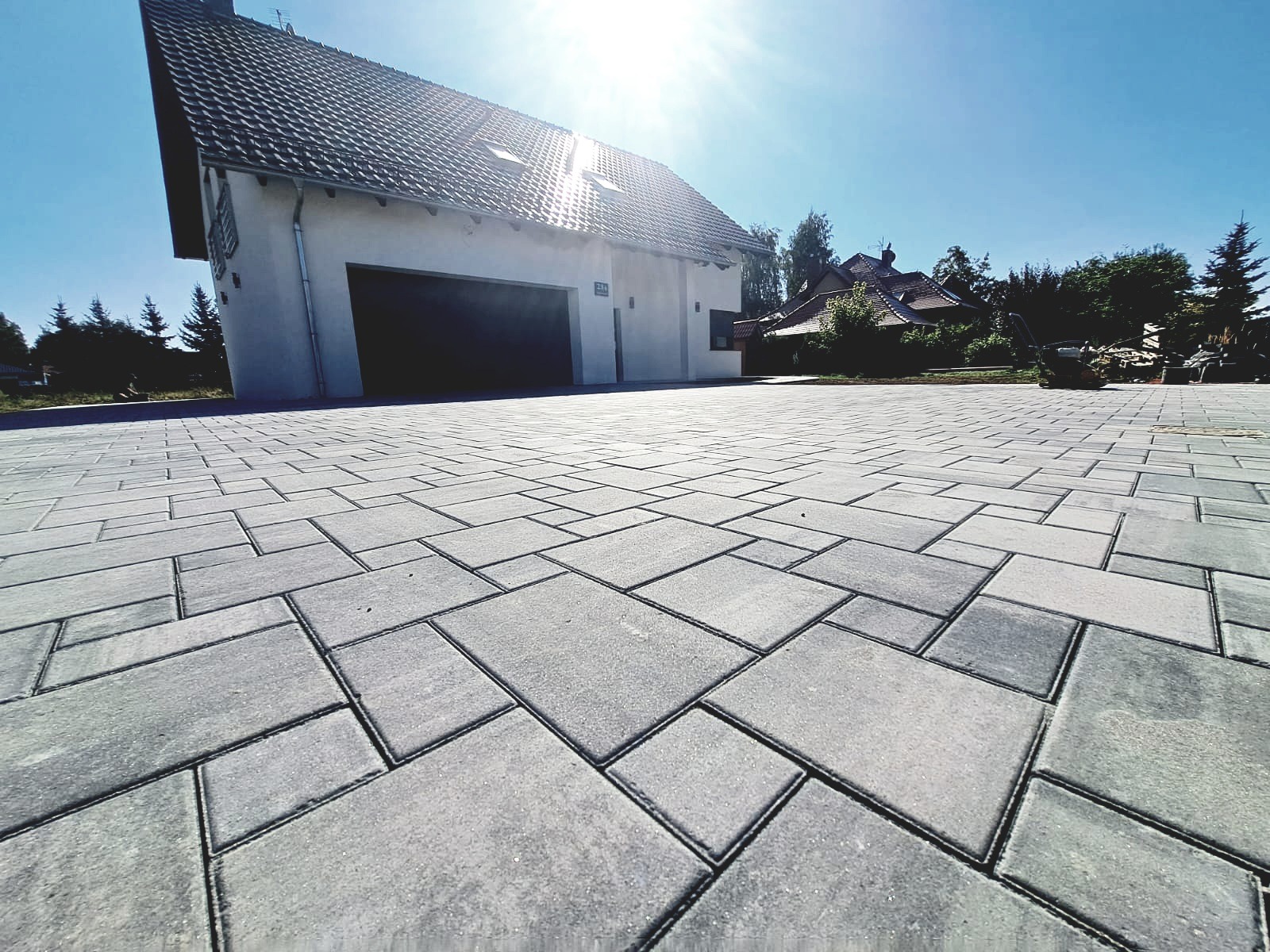 Nowo ułożona, szara kostka brukowa o nieregularnym wzorze przed nowoczesnym domem z garażem, widok z niskiej perspektywy w słoneczny dzień.