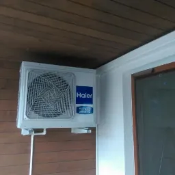 Zamontowana jednostka zewnętrzna klimatyzacji Haier Multi R32 Inverter na brązowej elewacji drewnianej, widoczna rura odprowadzająca.