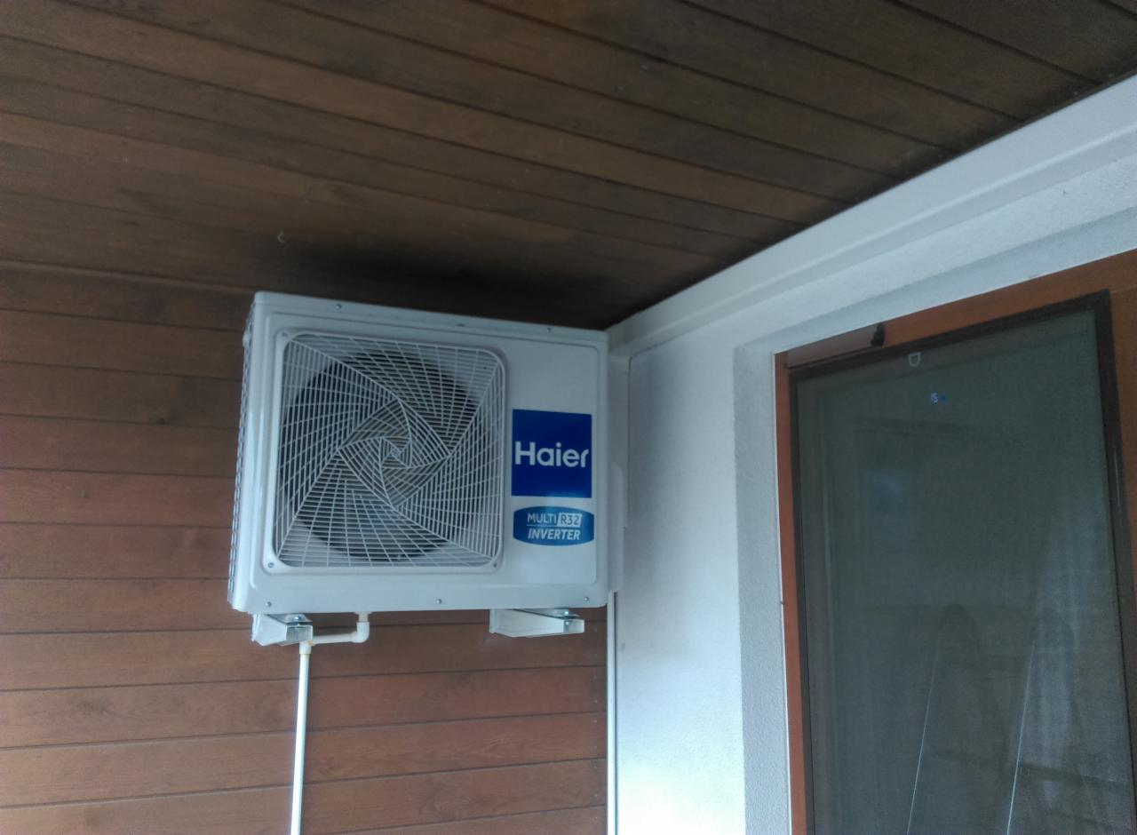 Zamontowana jednostka zewnętrzna klimatyzacji Haier Multi R32 Inverter na brązowej elewacji drewnianej, widoczna rura odprowadzająca.