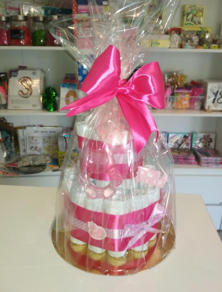 Tort z pieluch w celofanie, ozdobiony różową kokardą i wstążkami, prezent dla noworodka.
