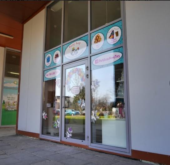 Fasada lokalu Party Shop w Nowym Targu, oklejona grafikami balonów, słodyczy i jednorożców, widok z zewnątrz w słoneczny dzień.
