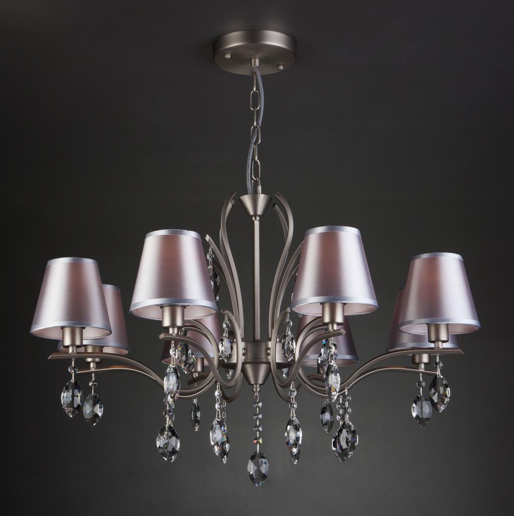 Srebrny żyrandol z sześcioma abażurami w kolorze mauve i kryształowymi zawieszkami na tle ciemnoszarej ściany.