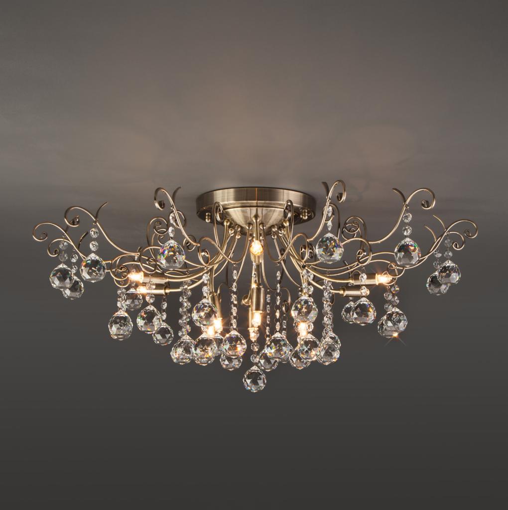 Sufitowa lampa w stylu vintage z metalową konstrukcją w kolorze starego złota i szklanymi kryształkami, zamontowana na szarym suficie.