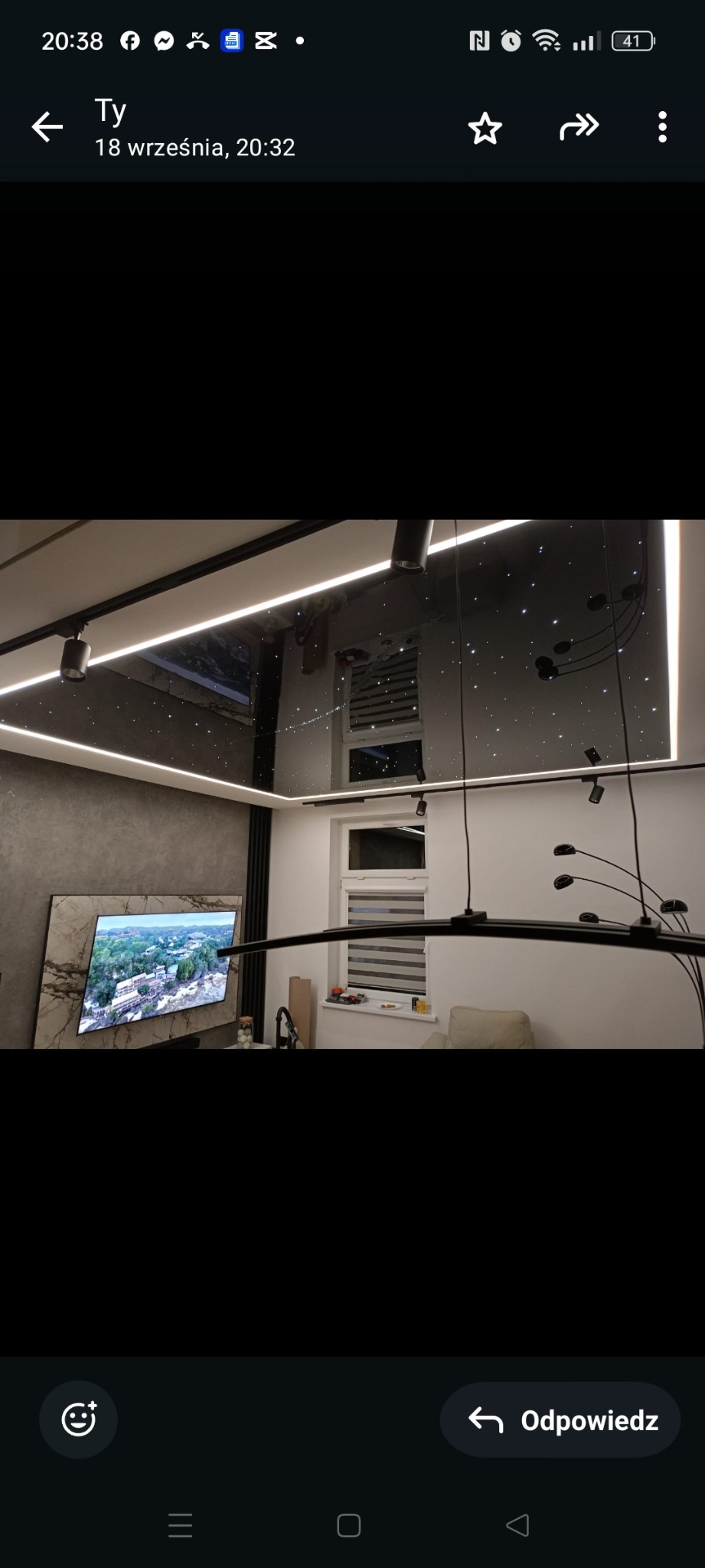 Salon z czarnym, lustrzanym sufitem z efektem gwiazd, oświetlonym listwami LED i reflektorami punktowymi, szara ściana z telewizorem w ozdobnej ramie, nowoczesna lampa łukowa