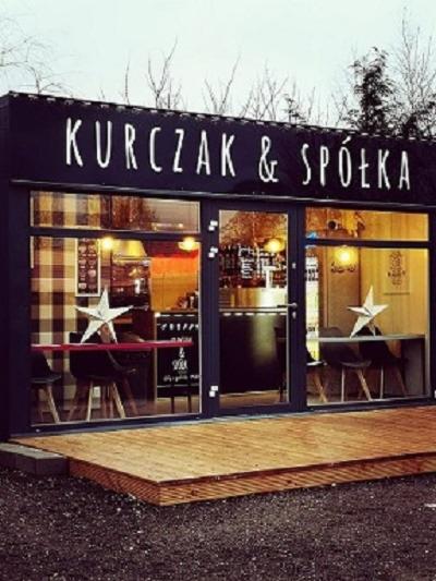 Fasada małej restauracji 'Kurczak & Spółka' w kontenerze z drewnianym tarasem, widoczne stoliki z gwiazdami w oknie, wnętrze z menu i napojami.