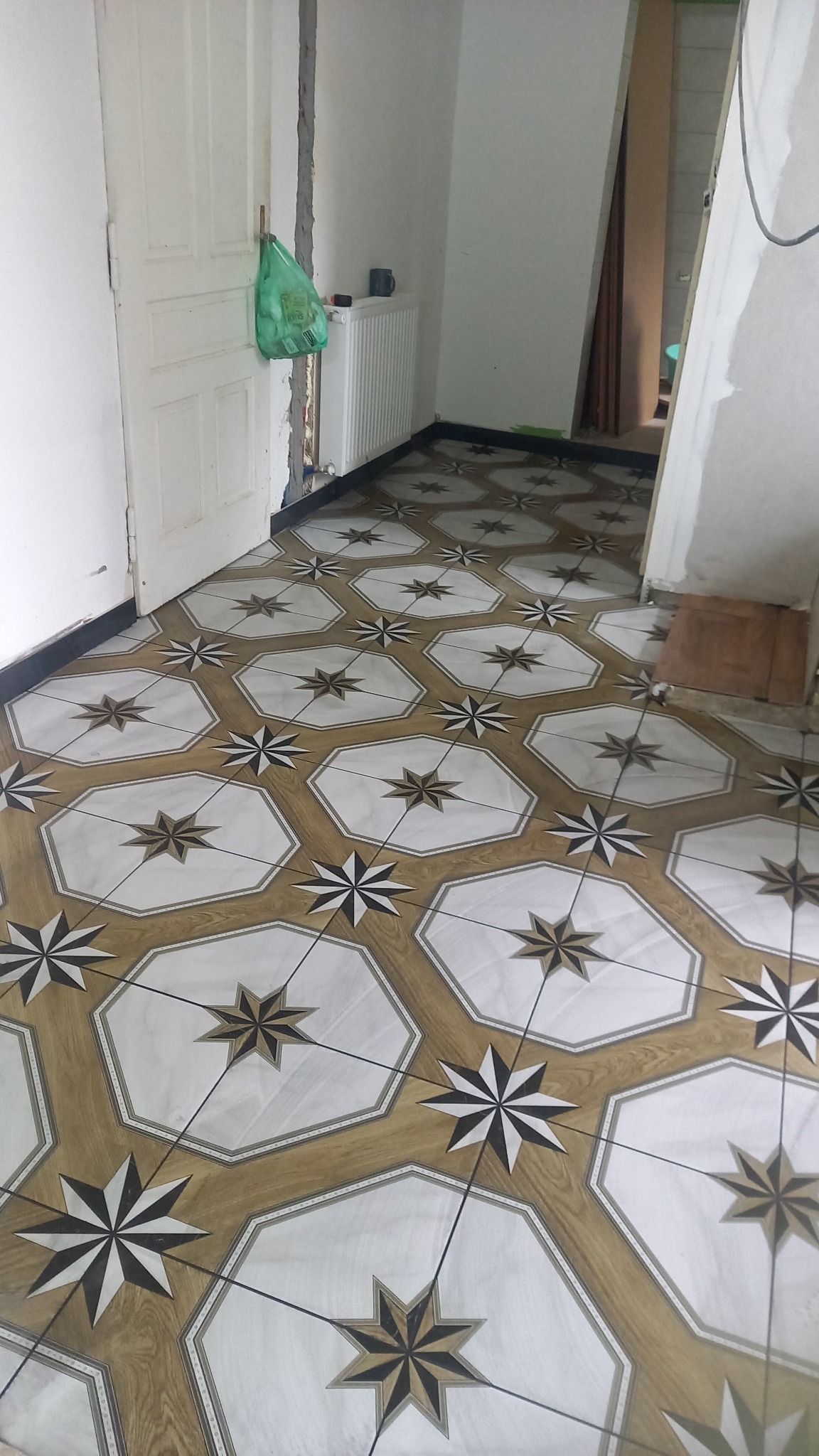 Ułożona podłoga z płytek w kształcie ośmiokątów z motywem gwiazd, widoczne niedokończone ściany i grzejnik.