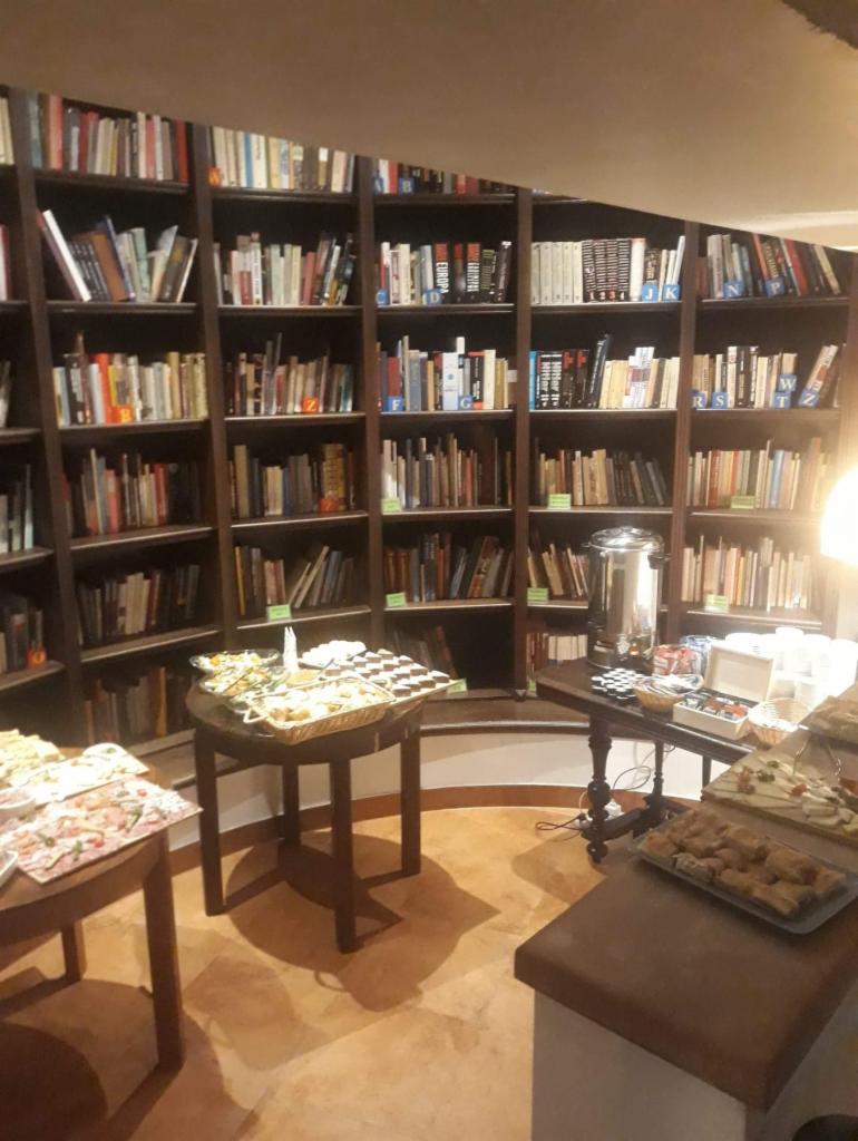 Stół z przekąskami i napojami na tle obszernej biblioteczki w ciepłym oświetleniu, przygotowany na przyjęcie.