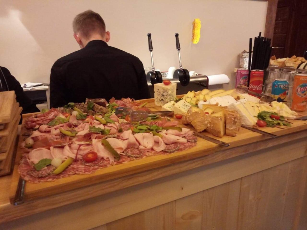 Deska wędlin i serów z dodatkami, napoje w puszkach i szklankach, przygotowana na drewnianym stole podczas obsługi imprezy.