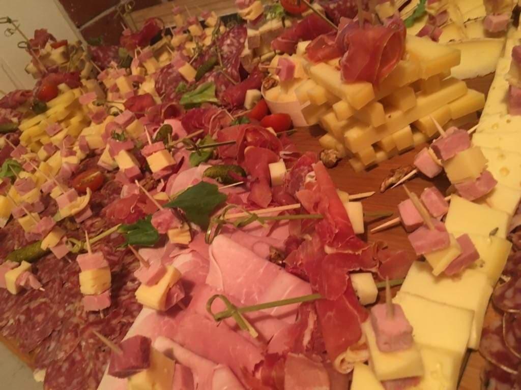 Bogato zastawiony stół z przekąskami: szaszłyki z sera i wędliny, plasterki salami, szynki i warzywa, całość w ciepłej tonacji oświetlenia.