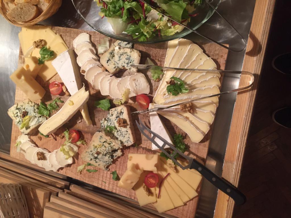 Deska serów z różnymi gatunkami, orzechami włoskimi, pomidorkami cherry i sałatą, serwowana ze szczypcami do nakładania.