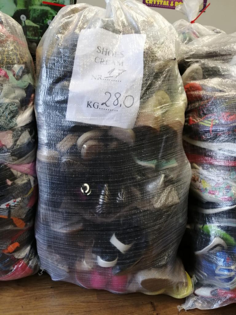 Worek foliowy wypełniony obuwiem, z etykietą 'SHOES CREAM NR. 17 KG 28,0', stojący obok innych worków z obuwiem.