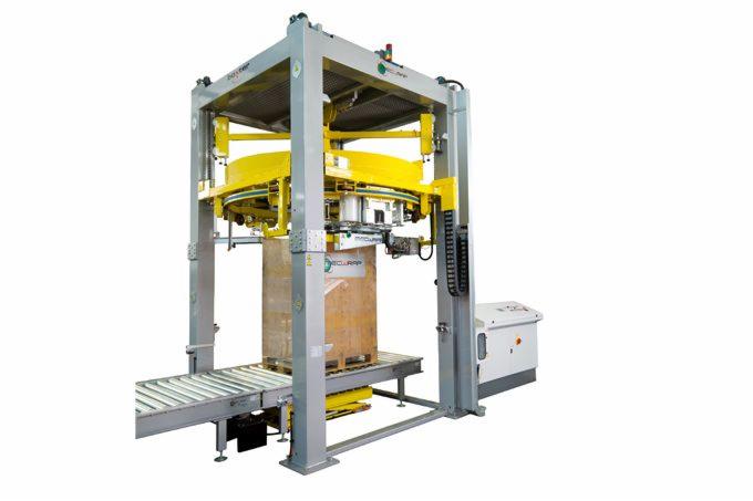 Automatyczna owijarka palet z żółtym pierścieniem obrotowym, umieszczona nad paletą z towarem na linii produkcyjnej, widoczna szafa sterownicza z boku.