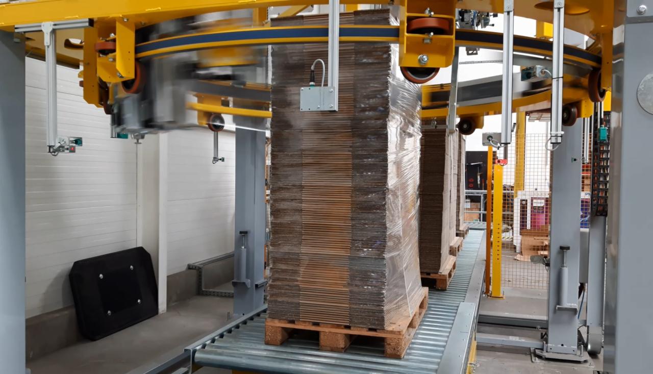 Automatyczna owijarka palet folią stretch: palety z kartonami owinięte folią na linii produkcyjnej.
