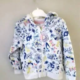 Dziecięca bluza z kapturem, biała z motywem kwiatów, motyli i królików, zawieszona na białym wieszaku.