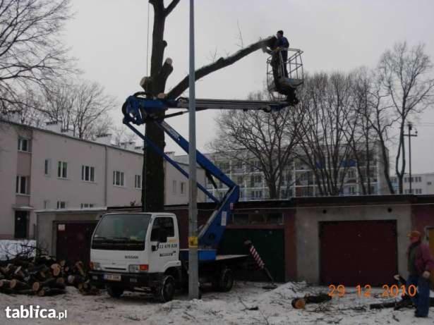 Przycinanie drzewa z podnośnika koszowego na tle miejskiego krajobrazu. Ścięte gałęzie leżą na śniegu. Biała ciężarówka z podnośnikiem.