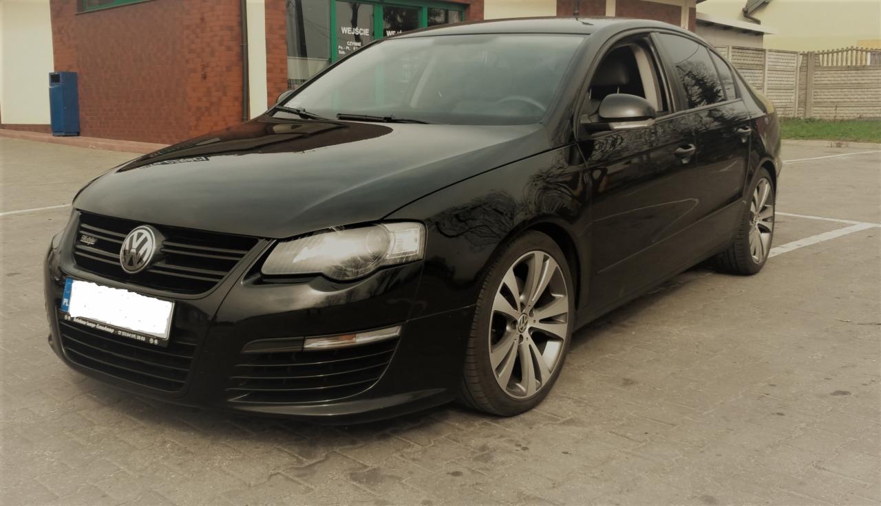 Czarny samochód osobowy marki Volkswagen, model Passat R36, zaparkowany na betonowym placu przed budynkiem.
