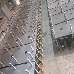 Usługi ślusarsko-spawalnicze Rafał Hałupka - Metalowe płyty z przymocowanymi śrubami, ułożone jedna na drugiej. Widoczne otwory w płytach i spawane elementy konstrukcyjne. Płyty przygotowane do dalszej obróbki.