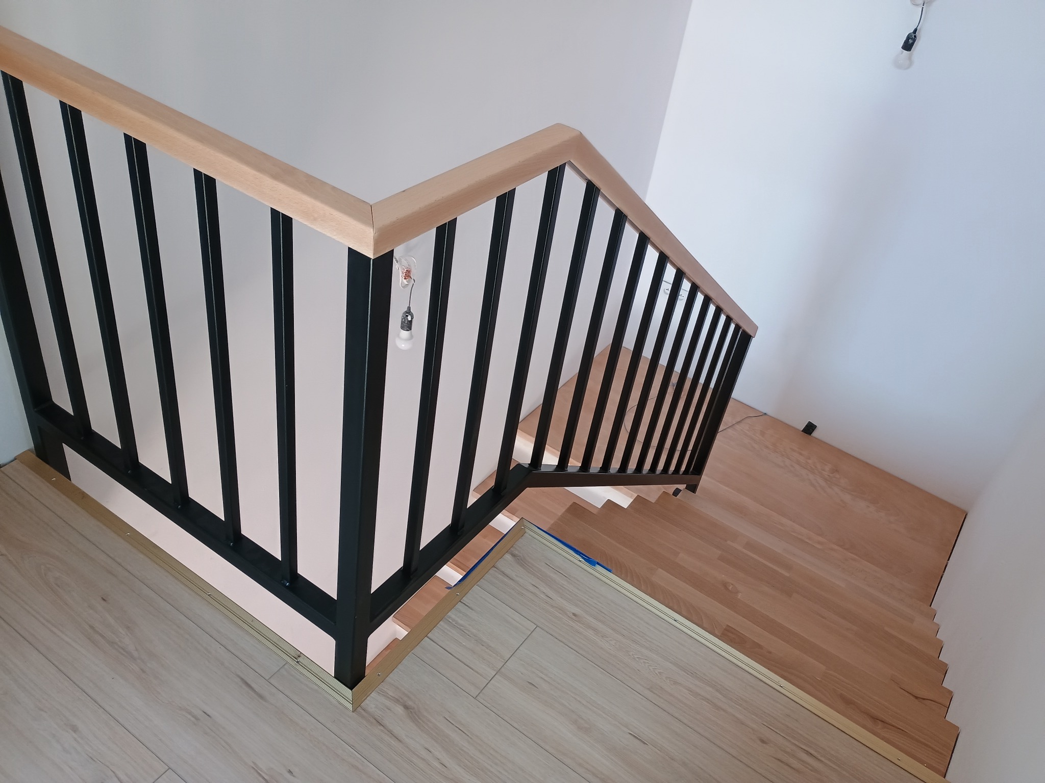 Nowoczesne schody z drewnianymi stopniami i czarną metalową balustradą z jasnym drewnianym poręczą, widok z góry, minimalistyczny design.