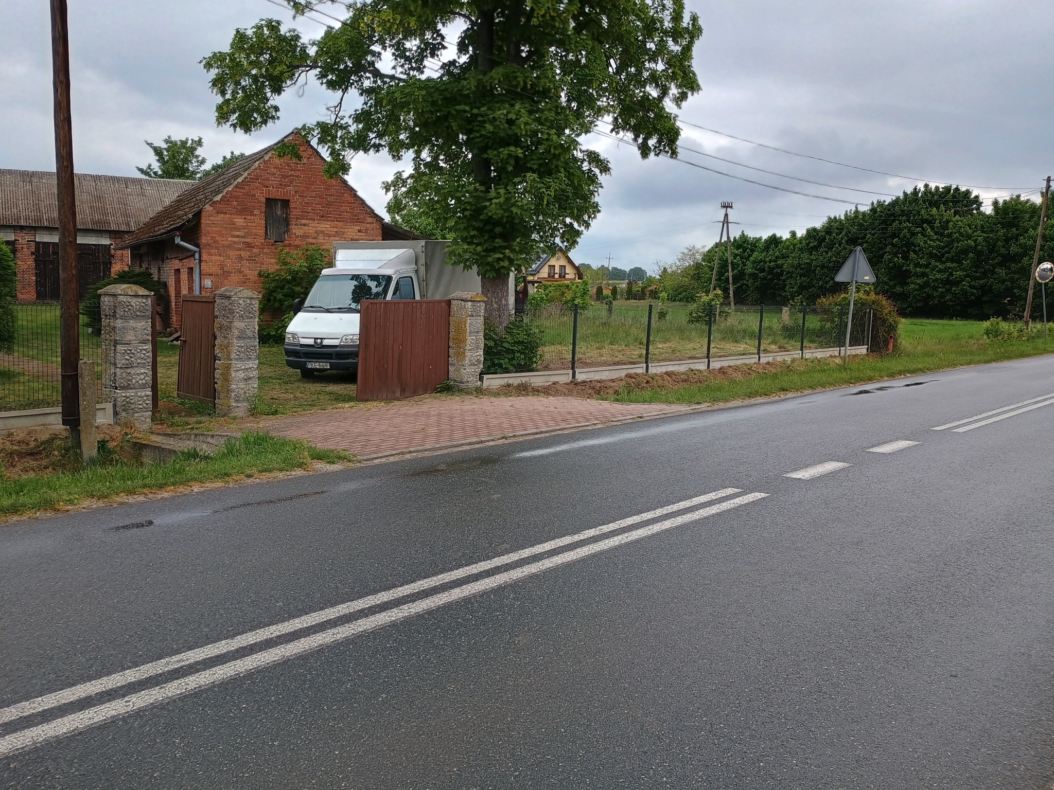 Nowoczesne ogrodzenie panelowe z podmurówką w Rychtalu, widoczne z perspektywy ulicy. Brama wjazdowa z drewnianymi skrzydłami i kamiennymi słupkami.