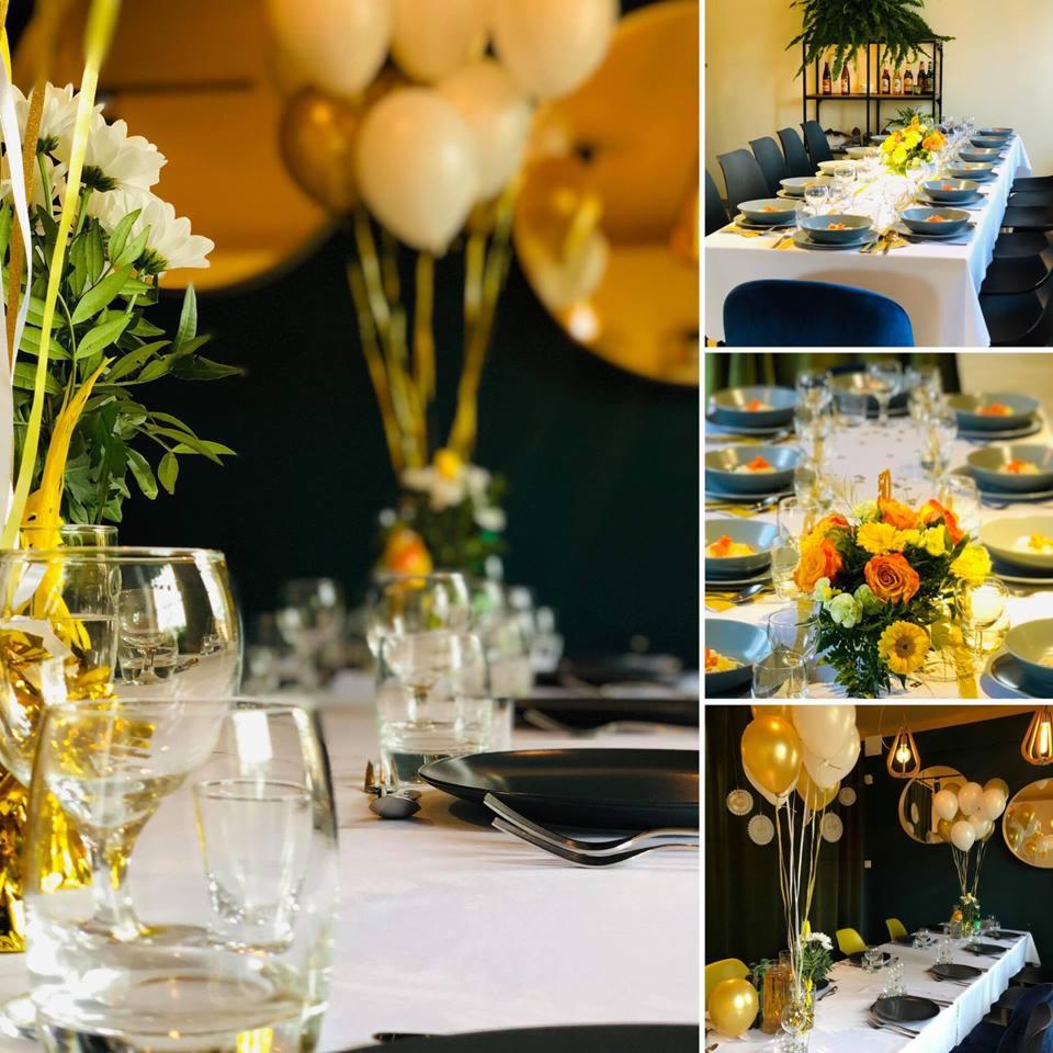 Uroczysty stół z białym obrusem, czarnymi talerzami, bukietami białych i żółtych kwiatów w wazonach, szklankami i kieliszkami, dekoracjami ze złotych wstążek i balonów w kolorach złota i bieli...