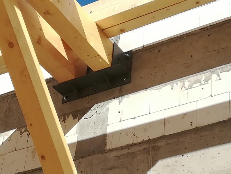 Drewniana konstrukcja dachu zamocowana do ściany z betonu komórkowego za pomocą stalowego łącznika na śruby.