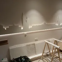 Podświetlany, wycięty w ścianie motyw panoramy miasta z listwą LED, widoczne narzędzia i elementy montażowe w trakcie prac wykończeniowych.
