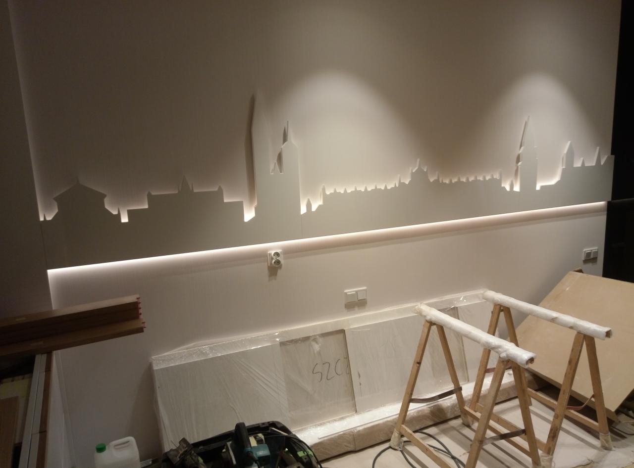 Podświetlany, wycięty w ścianie motyw panoramy miasta z listwą LED, widoczne narzędzia i elementy montażowe w trakcie prac wykończeniowych.