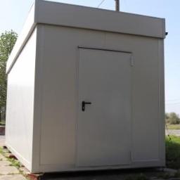 KAMP KONTENER S.C. PRODUCENT KONTENERÓW - Szary, prostokątny kontener mieszkalny z pojedynczymi drzwiami, umieszczony na niewielkich fundamentach, widoczny z perspektywy lekko z dołu.