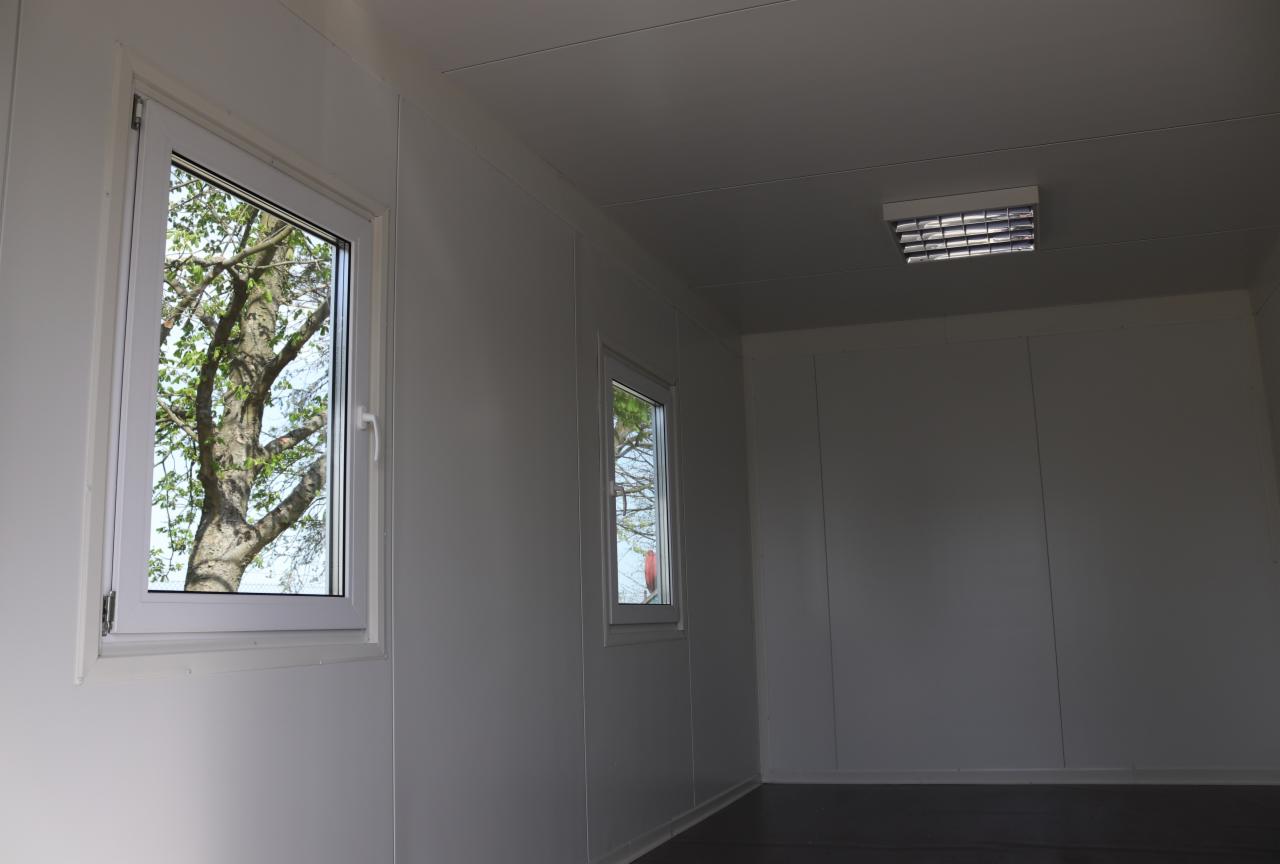 Wnętrze rozbudowanego domu z dwoma oknami z widokiem na drzewa i sztucznym oświetleniem sufitowym.