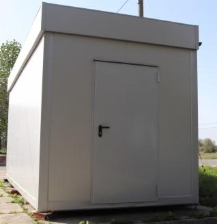 Szary, prostokątny kontener mieszkalny z pojedynczymi drzwiami, umieszczony na niewielkich fundamentach, widoczny z perspektywy lekko z dołu.