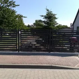 Nowoczesna, pozioma, metalowa brama wjazdowa w kolorze antracytowym, zamontowana przed domem jednorodzinnym z kostki brukowej.