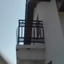 Balkon z czarną metalową balustradą o wzorze greckim, przymocowaną do ściany budynku, widoczne elementy konstrukcyjne.