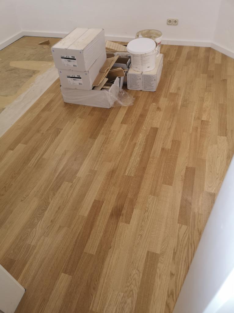 Ułożona, jasna podłoga z paneli drewnopodobnych w trakcie prac wykończeniowych, z widocznymi materiałami i narzędziami w tle.