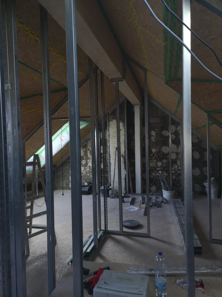 Montaż metalowej konstrukcji ścian działowych z płyt karton-gips na poddaszu, widoczne profile, izolacja oraz fragmenty starego muru.