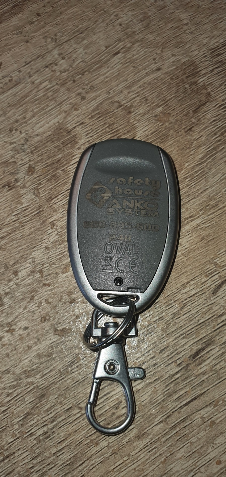 Szary pilot do systemu alarmowego z metalowym karabińczykiem, leżący na drewnianej powierzchni.
