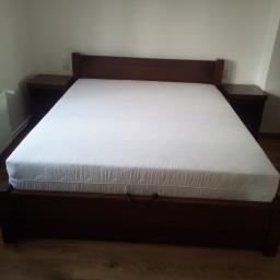 MEBLO-STYL JACEK CHACHUŁA - Ciemnobrązowe łóżko z drewnianą ramą i zagłówkiem, z białym materacem, szafki nocne po bokach, na drewnianej podłodze.