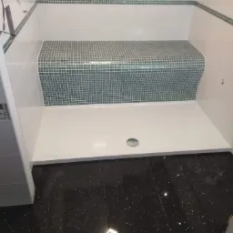 Nowoczesna kabina prysznicowa z brodzikiem, mozaiką na siedzisku i błyszczącą, czarną podłogą z efektem gwiazd.