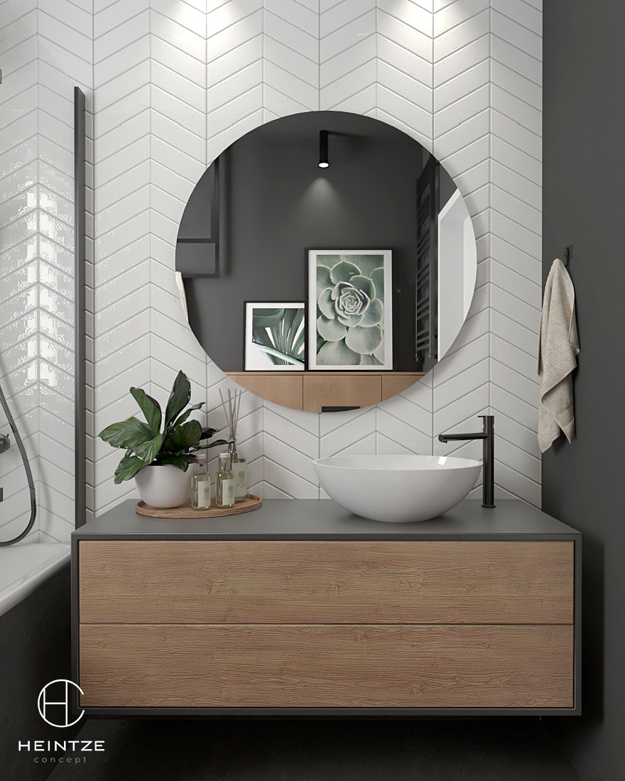 Nowoczesna łazienka z białą umywalką nablatową, czarną armaturą i lustrem w okrągłej ramie, na tle ściany z białych płytek ułożonych w jodełkę, z drewnianą szafką pod umywalką i dekoracyjnymi...