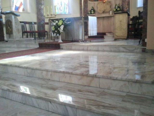 Kamienne schody prowadzące do marmurowego ołtarza w kościele, z widocznymi refleksami światła na polerowanej powierzchni.