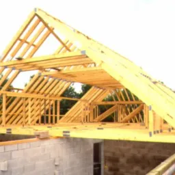 Wznoszenie drewnianej konstrukcji dachu z widocznymi wiązarami na murowanym budynku w trakcie budowy, z zielenią w tle.