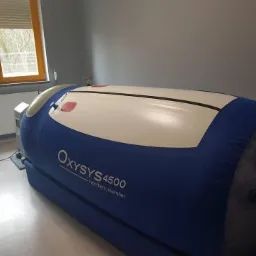 Oksygenowa komora hiperbaryczna Oxysys 4500 w jasnym pomieszczeniu z oknem, widok z boku.