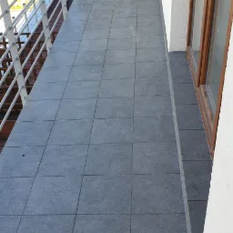 Szare płytki gresowe na balkonie z białą balustradą i ścianą, widok z góry.