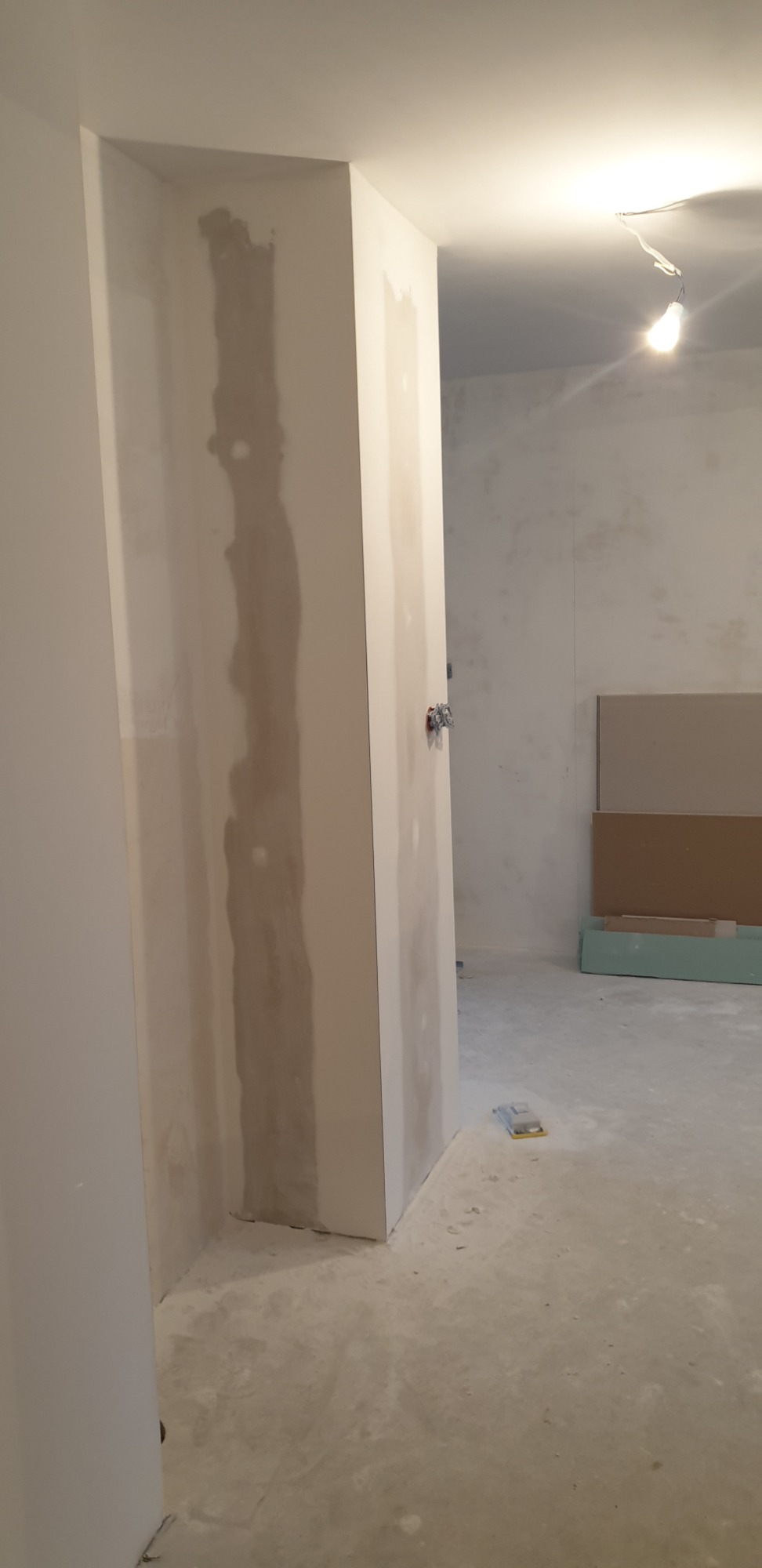 Wyrównywanie ściany płytą karton gips, widoczne łączenia zaszpachlowane gipsem, na podłodze poziomica.