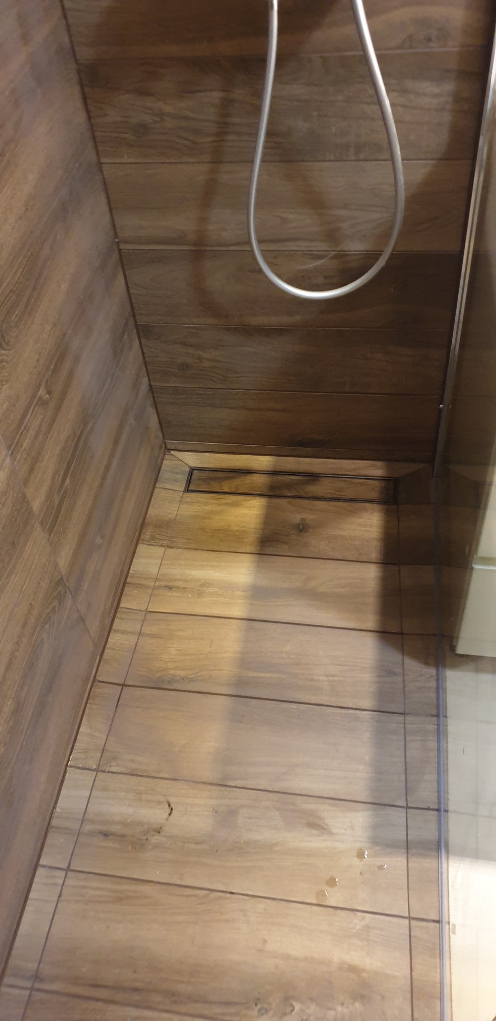 Ukończony prysznic typu walk-in z odpływem liniowym, wyłożony płytkami imitującymi drewno na ścianach i podłodze.