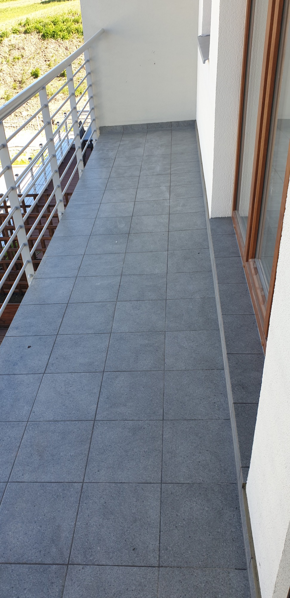 Szare płytki gresowe na balkonie z białą balustradą i ścianą, widok z góry.