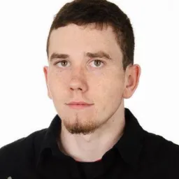 Portret młodego mężczyzny z krótkimi włosami i kozia bródką, ubrany w czarną koszulę z napisem 'SUPER 1958'.