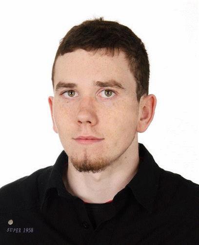 Portret młodego mężczyzny z krótkimi włosami i kozia bródką, ubrany w czarną koszulę z napisem 'SUPER 1958'.