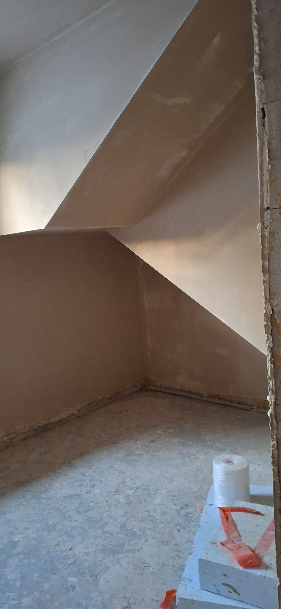 Wykończone ściany i sufit na poddaszu po nałożeniu gładzi. Widoczne załamania i skosy. Na podłodze resztki materiałów budowlanych. Surowy stan wykończenia.