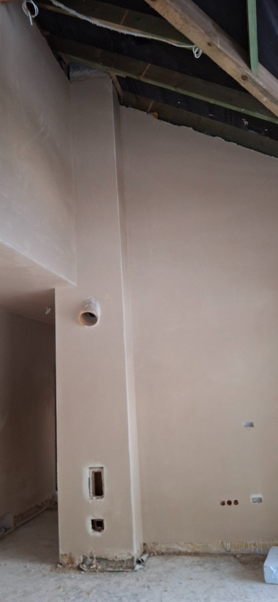 Świeżo nałożony tynk maszynowy na ścianach wewnętrznych budynku w trakcie remontu. Widoczne otwory instalacyjne i surowy strop.