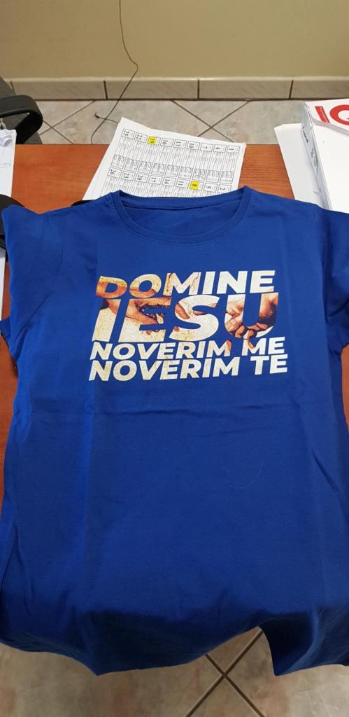 Niebieska koszulka z nadrukiem 'DOMINE IESU NOVERIM ME NOVERIM TE' leżąca na biurku obok kalendarza.